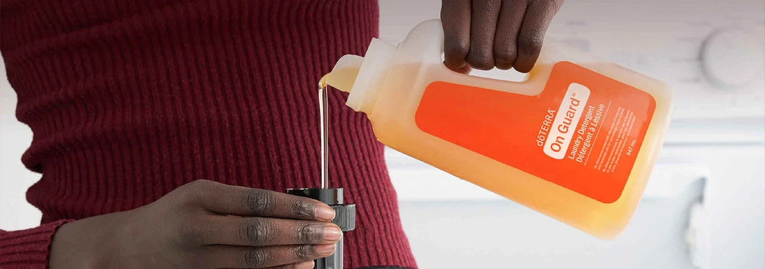 Lessive On Guard dōTERRA versée dans un bouchon doseur, devant un lave-linge