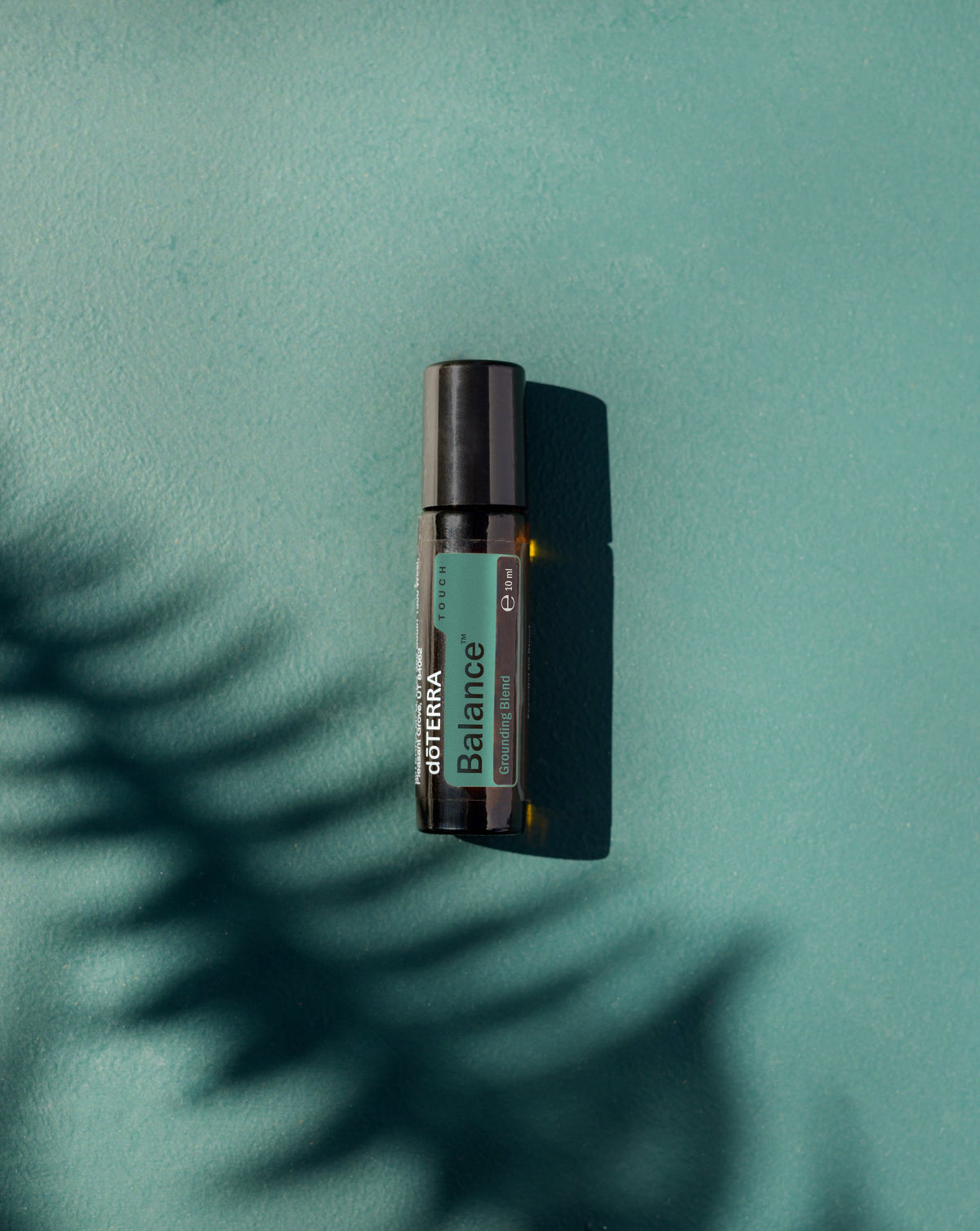 Balance Touch dōTERRA, flacon sur fond vert avec ombre de fougère
