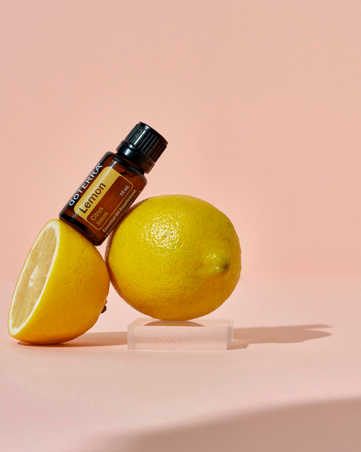 Citron huile essentielle dōTERRA, posé sur un citron, fond rose