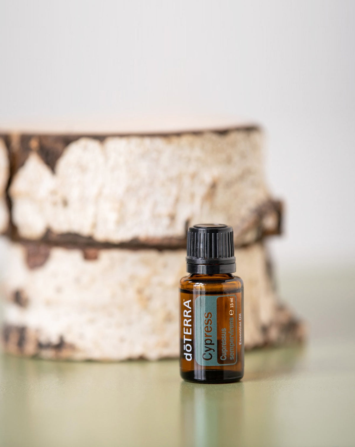 Cyprès dōTERRA, flacon devant une bûche de bouleau