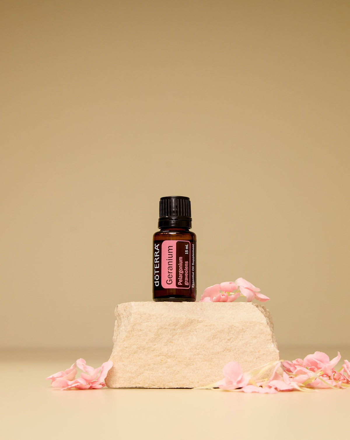 Géranium huile essentielle dōTERRA, flacon sur une pierre et pétales roses