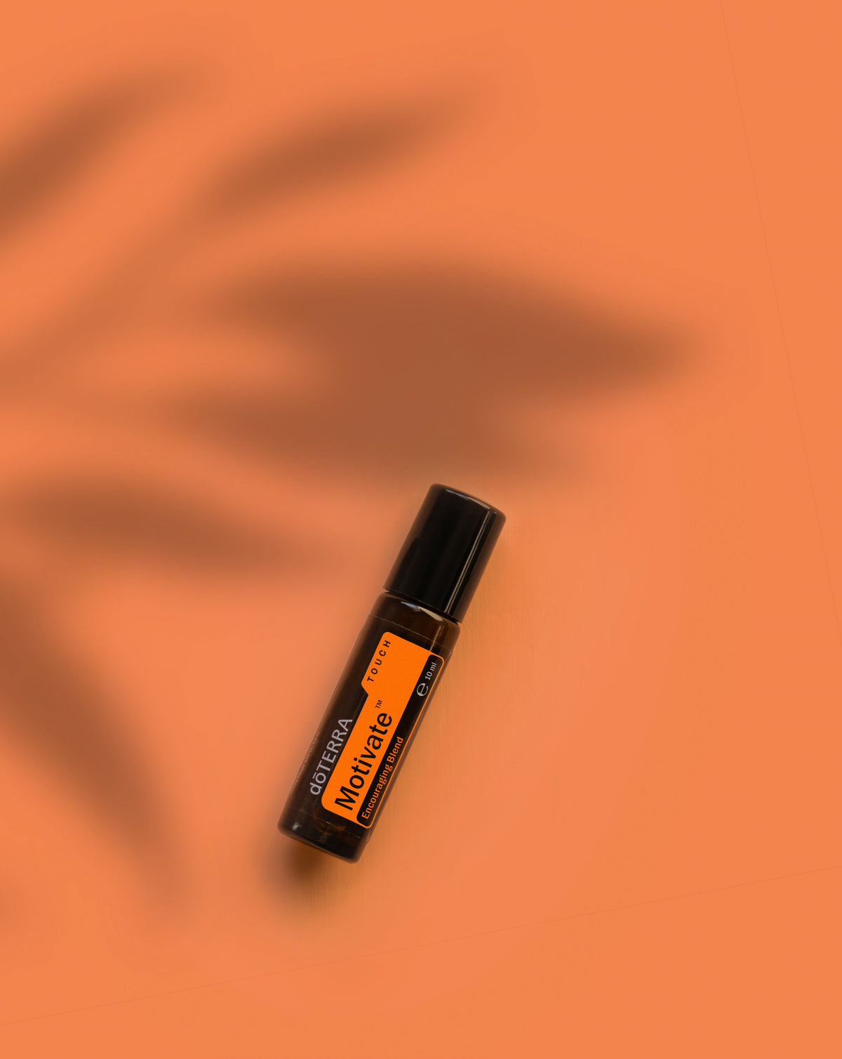Motivate Touch dōTERRA, flacon sur fond orange avec ombre de feuillage