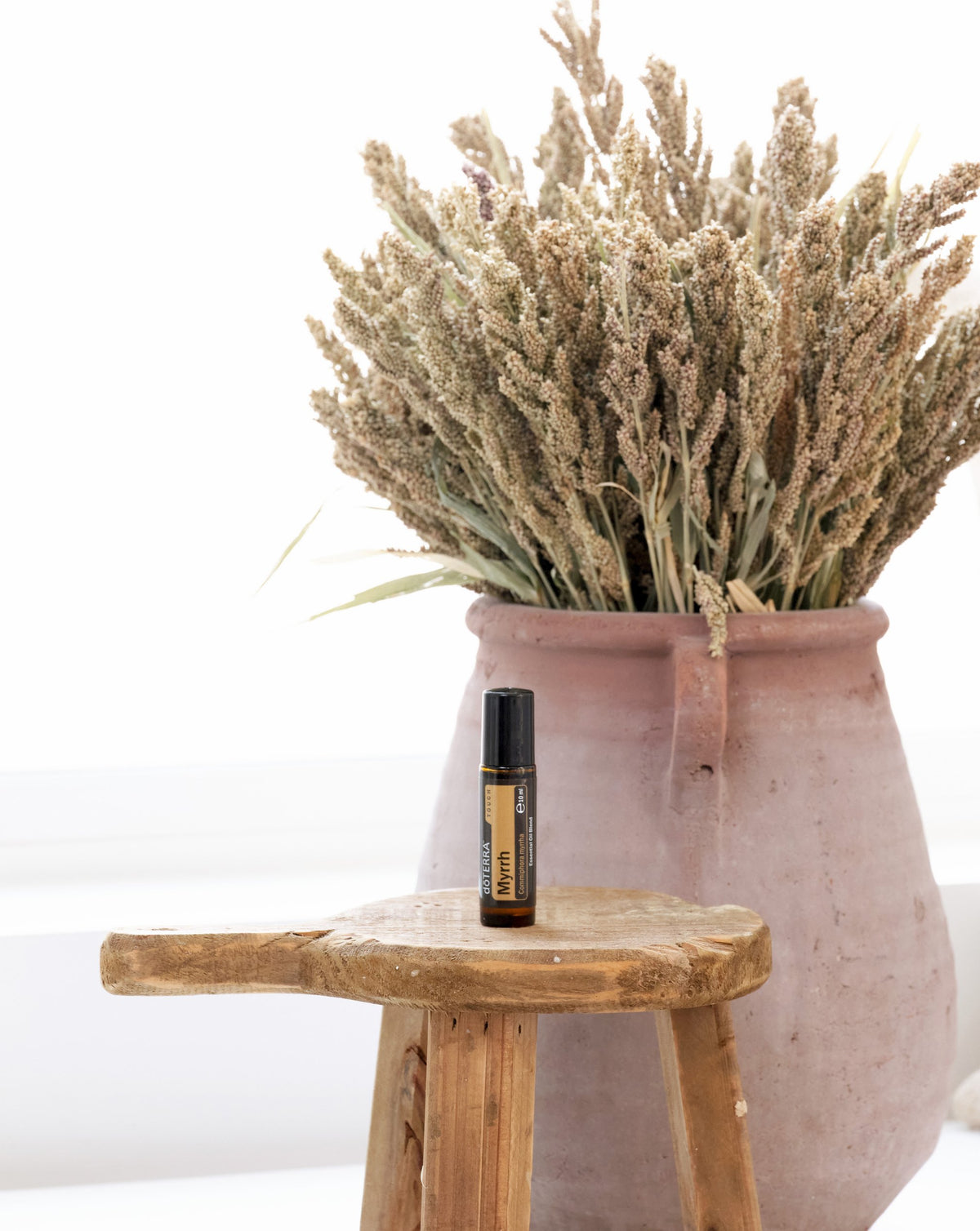 Myrrhe Touch dōTERRA, flacon sur un tabouret en bois près d'un bouquet séché