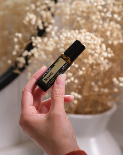 Myrrhe Touch dōTERRA, flacon à bille tenu devant des fleurs séchées