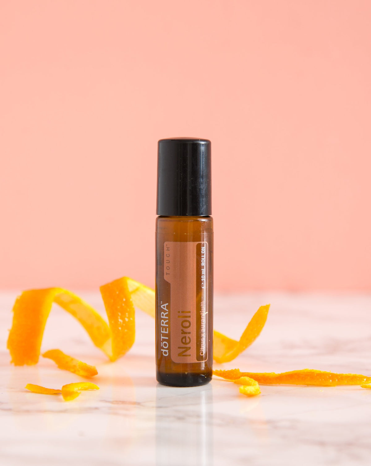 Néroli Touch dōTERRA, flacon et zestes d'orange sur fond rose