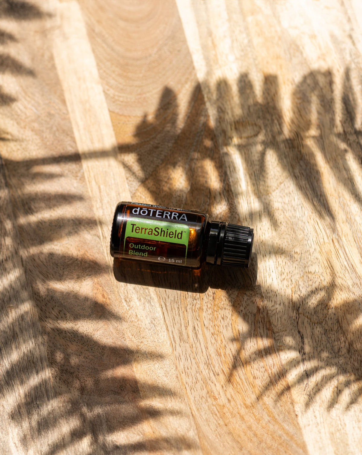 TerraShield dōTERRA, flacon couché sur du bois à l'ombre d'une fougère